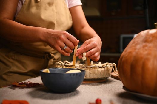 Close-up of a housewife in beige chef's apron, decorating the classic American homemade festive pie with a crunchy pastry lattice. Thanksgiving Day. Making tasty pumpkin apple pie with flaky crust.