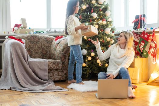 cheerful teenage girl and mother celebrating christmas at home and communicating online.
