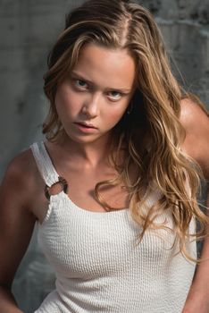 Debonair blonde girl sitting at sandy beach in autumn sunset. Outdoor portrait of pretty curly fashionable girl in a white bikini