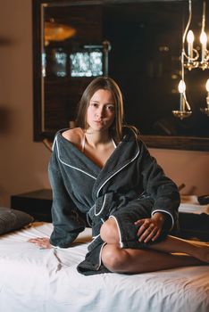 Young charming girl in a gray bathrobe waiting for procedure. beautiful woman spending time at modern spa cabinet for relaxing. Soft yellow light