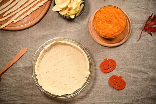 Still life. Flat lay. Food background. A rolled pastry dough in a baking dish and fresh ingredients for making pumpkin apple Thanksgiving pie. Branch with viburnum berries on a linen tablecloth