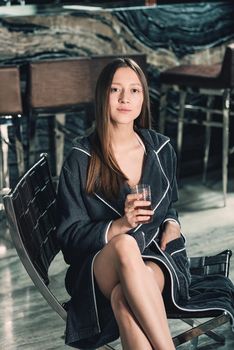 Portrait of young beautiful woman relaxing in a chair in a bathrobe with a detox drink in a hand. Luxery spa center. look at the camera