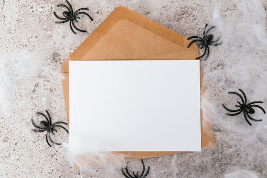 Halloween festival party, greeting card with mockup copy space. Halloween holiday concept. Halloween decorations, spider, web and empty blank paper on grey background.