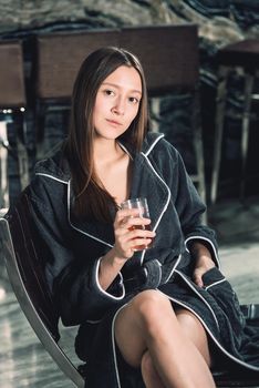 Portrait of young beautiful woman relaxing in a chair in a bathrobe with a detox drink in a hand. Luxery spa center. look at the camera