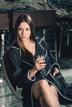 Portrait of young beautiful woman relaxing in a chair in a bathrobe with a detox drink in a hand. Luxery spa center. look at the camera