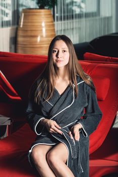 Portrait of young beautiful woman relaxing in a chair in a bathrobe with a detox drink in a hand. Luxery spa center