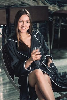 Portrait of young beautiful woman relaxing in a chair in a bathrobe with a detox drink in a hand. Luxery spa center. look at the camera