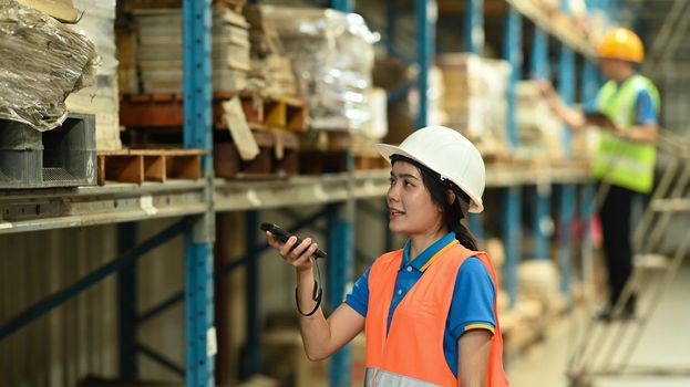 Young woman warehouse worker using barcode scanner checking stock on the shelves in a large warehouse.