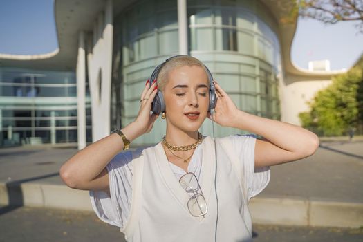Young beautiful girl with short white hair happy and dancing in the street with headphones. High quality photo