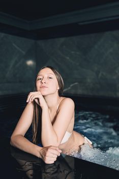 Sexy beautiful caucasian woman relaxing in a pool with jacuzzi. Dark room. Poor lighting.