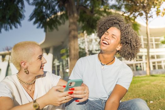 Afroamerican and caucasian couple looking the phone listening to music and laughing in the city. High quality photo. Multicultural group.