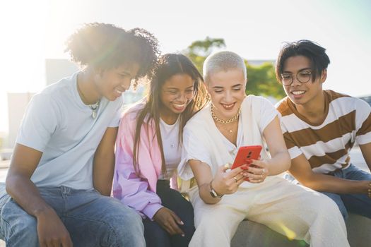 Group of happy teenage friends looking the phone and laughing in the city street with sun light flare. High quality photo. Multicultural group.