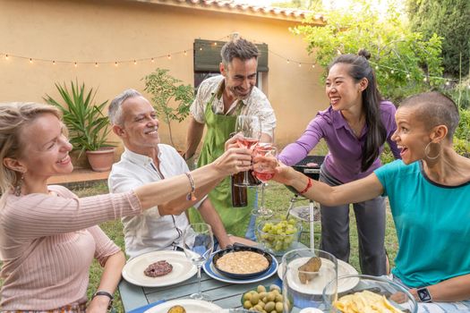 Multiracial middle aged friends eating, celebrating and toasting together in summer barbecue party. High quality photo