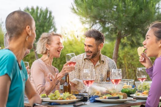 Happy friends laughing with big smile around the table in a summer diner. Smiling people eating at house patio. Smiles, cheerfulness concept. High quality photo