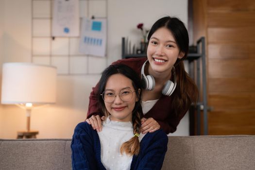 Two asian women having nice lively activity in living room on sofa in cozy interior.