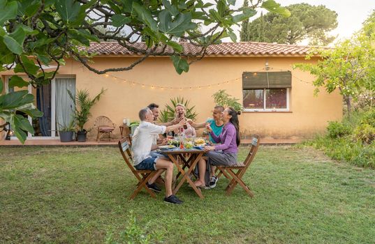 Happy friends dining and tasting together in garden in barbecue dinner party in summer. Smiling people eating at house patio. Smiles, cheerfulness concept. High quality photo