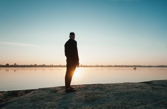 Suicide minds. silhouette of depressed young man holding gun standing near water.