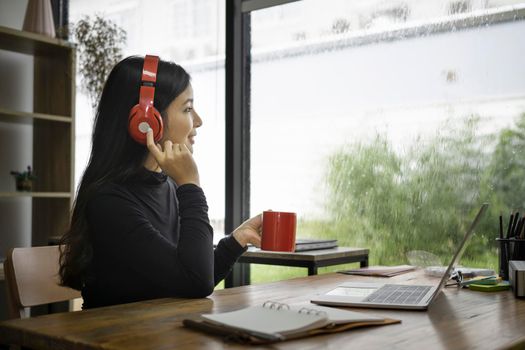 Young asian woman enjoy drinking coffee and listening to music with headphone.