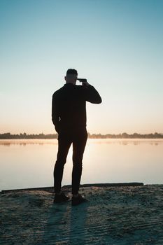 Suicide minds. silhouette of depressed young man holding gun near his head standing near water.