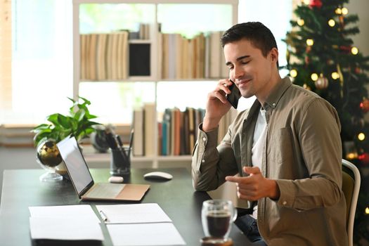 Handsome man talking on mobile phone while sitting in modern home office.