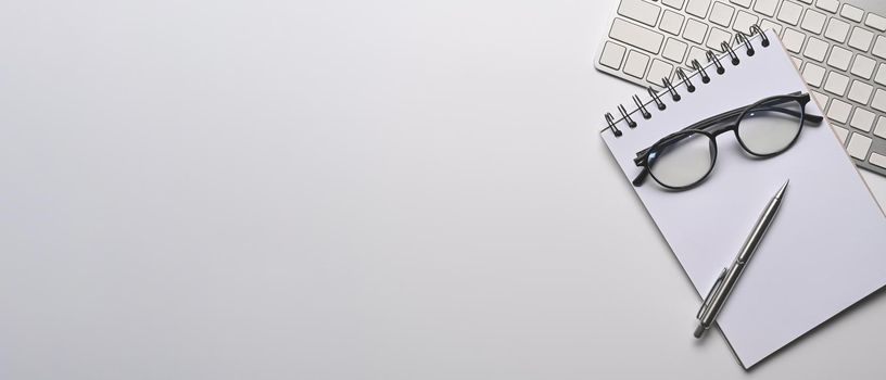 Empty notepad, eyeglasses, keyboard and pen on white office desk. Copy space.