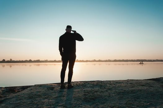 Suicide minds. silhouette of depressed young man holding gun near his head standing near water.