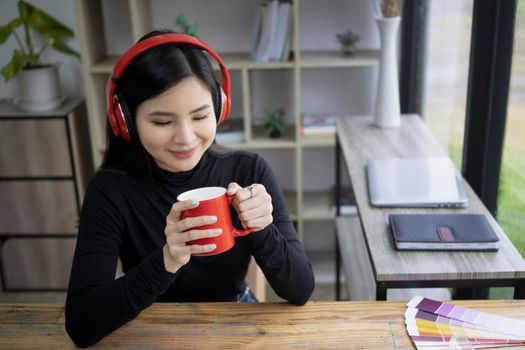 Smiling creative woman wearing headphone and holding red coffee cup.