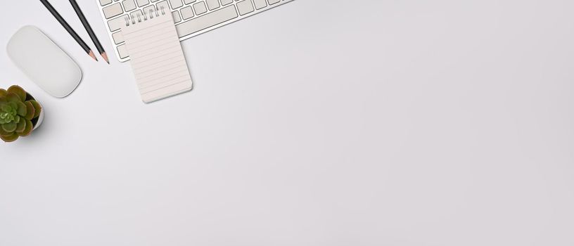 Top view minimal workspace with notebook, keyboard and potted plant on white table.