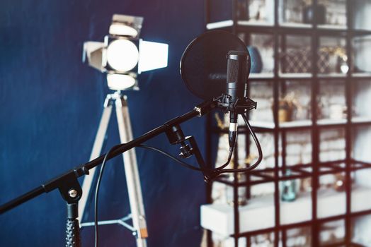 Close up studio condenser microphone with pop filter and anti-vibration mount live recording. Blue wall and decorative light on a background.