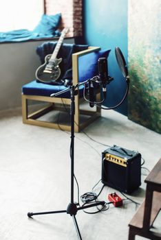 studio condenser microphone with pop filter and anti-vibration mount live recording. Blue wall, speaker and guitaron a background.