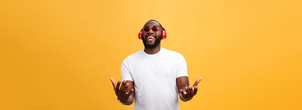 Handsome young African American man listening and smiling with music on his mobile device. Isolated over yellow background