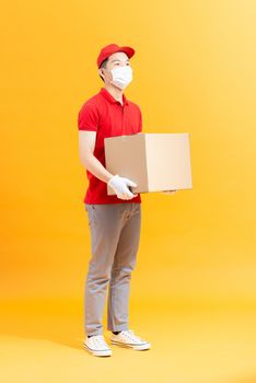 Courier in protective mask and medical gloves holding cardboard box to deliver