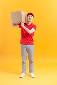 Young smiling logistic delivery man in red uniform holding the box on color background
