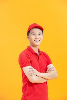 Smiling young handsome asian delivery man in red uniform standing with arm crossed