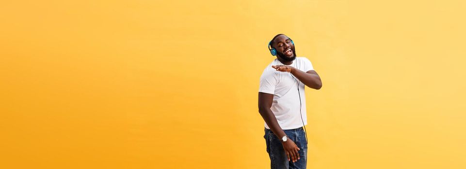 Full length portrait of a cherry young african american man listening to music with headphones and dancing isolated over yellow background.