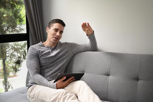 Young man wearing wireless earphones and having video call with digital tablet.