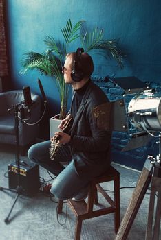 Close up of a man singer in a headphones with a guitar recording a track in a home studio. Man wearing sunglasses, jeans, black shirt and a jacket. side view