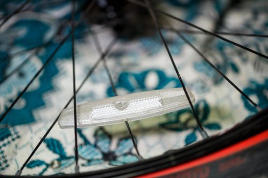 one plastic white reflector on gray metal spokes of a black wheel on a bicycle