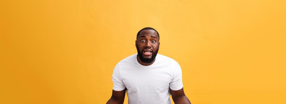 Portrait of african american man with hands raised in shock and disbelief. Isolated over yellow background