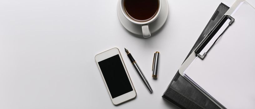 Mock up mobile phone, coffee cup and clipboard on white office desk.