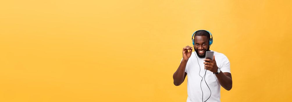 African American man with headphones listen and dance with music. Isolated on yellow background.