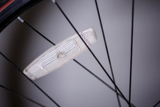 one plastic white reflector on gray metal spokes of a black wheel on a bicycle