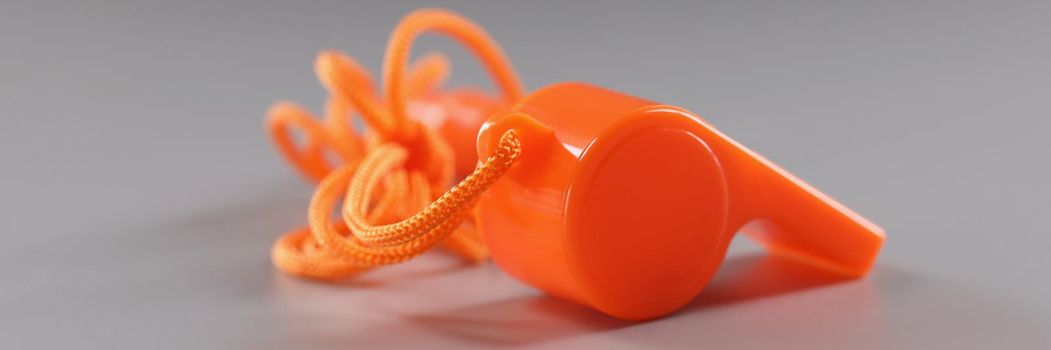 Close-up of orange sport whistle on grey surface, tool for school trainers. Side view of whistle, loud sound maker. Sport competition equipment concept