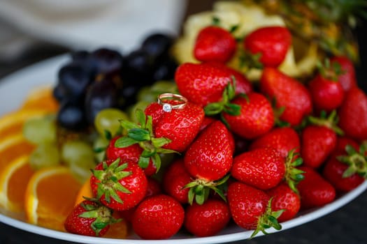 The wedding ring lies on a red ripe strawberry. Summer delicious berries