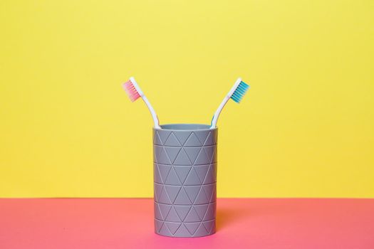 Two toothbrushes stand with a gray glass on a yellow background. Toothbrush concept for a couple, living together as the beginning of a family