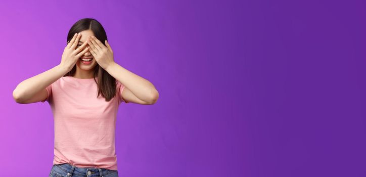 Girl waiting command open eyes, lively giggle smiling happily, cover eyes, peeking through fingers, anticipating cool surprise, laughing joyfully, awaiting present, stand purple background.