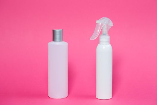 Two white bottles with shampoo for hair, body gel, spray for the skin on a pink background