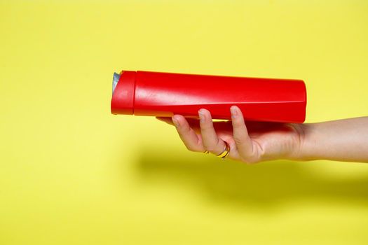 Red bottle in hands with gel shampoo or liquid soap on a yellow background