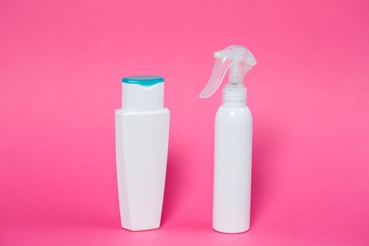 Two white bottles with shampoo for hair, body gel, spray for the skin on a pink background