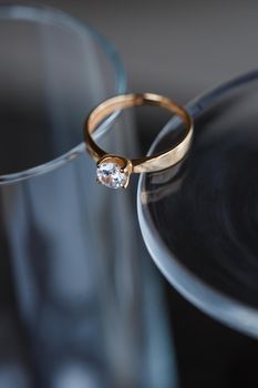 A wedding ring made of precious metal with a diamond stone lies in a glass